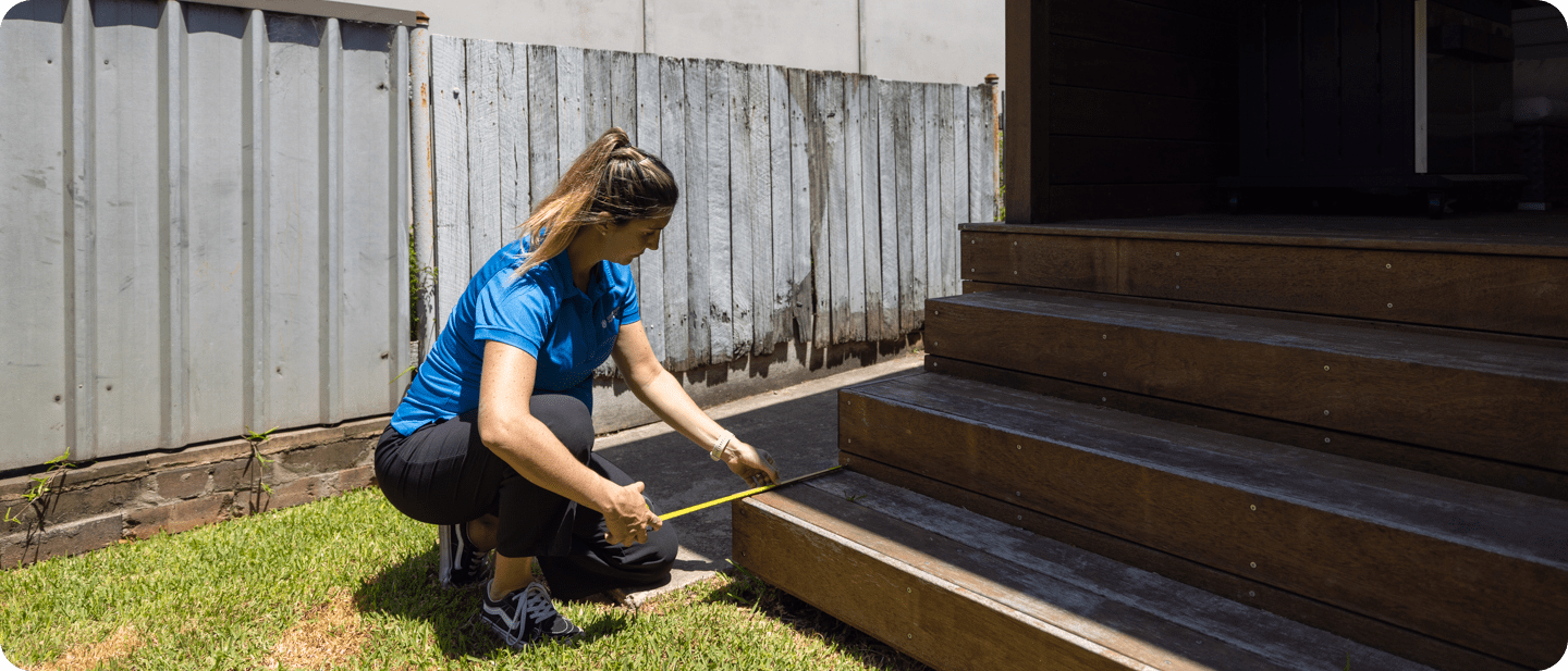 Person in a blue shirt measuring a wooden step with a tape measure.