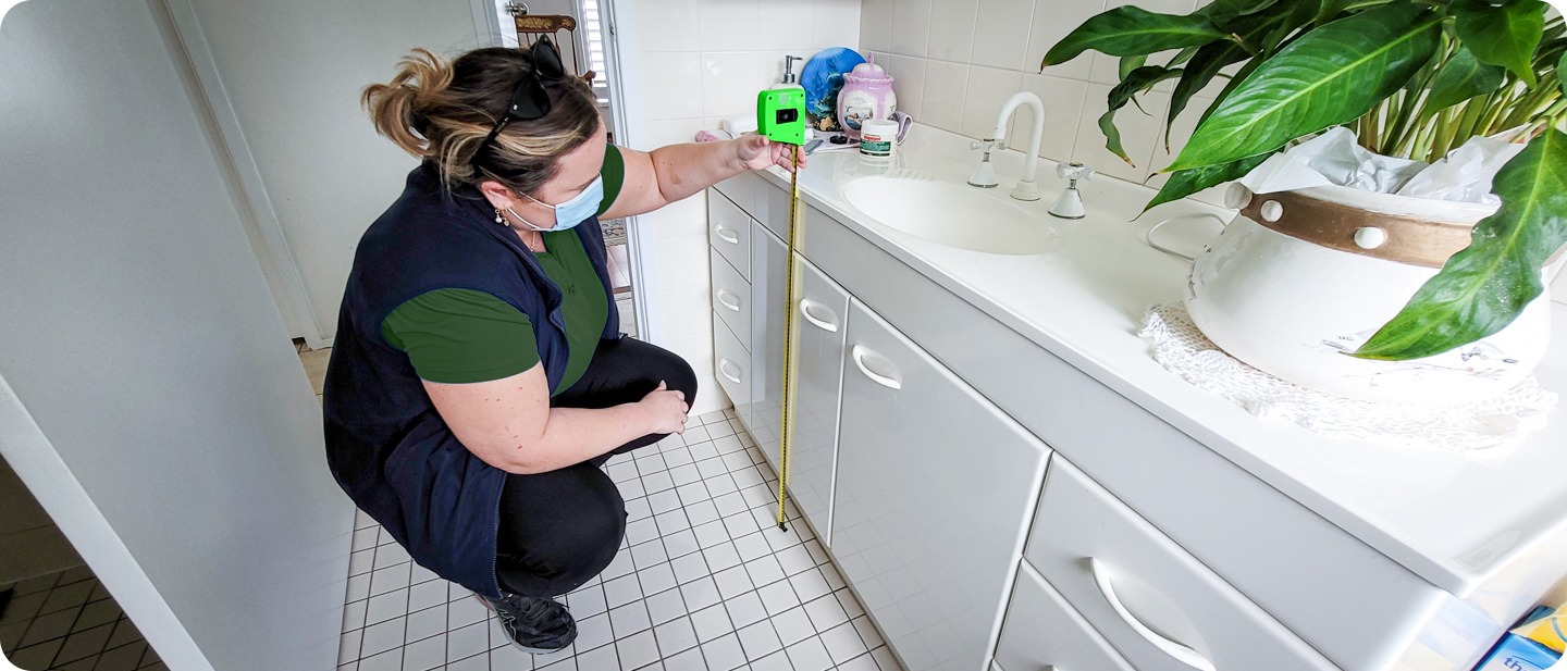 Person in a green shirt measuring the height of a bathroom vanity with a tape measure